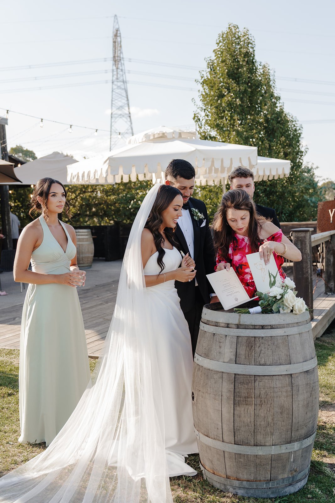 A couple holding hands at a wedding ceremony, standing in front of white flowers and a white wall.