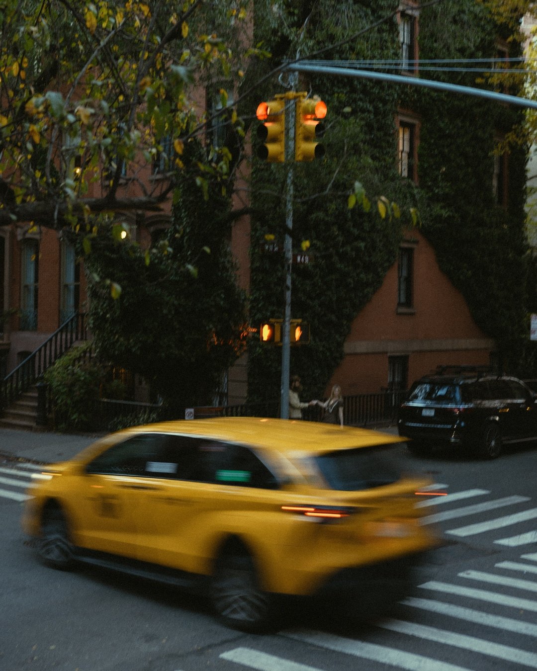 Couple walking with motion blur past yellow taxi in West Village