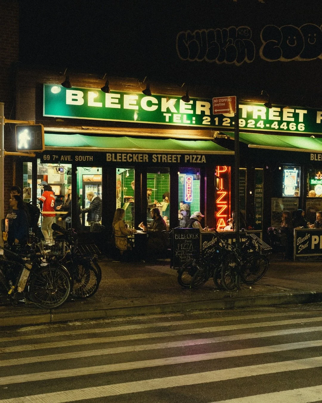 Couple eating pizza under Bleecker Street sign