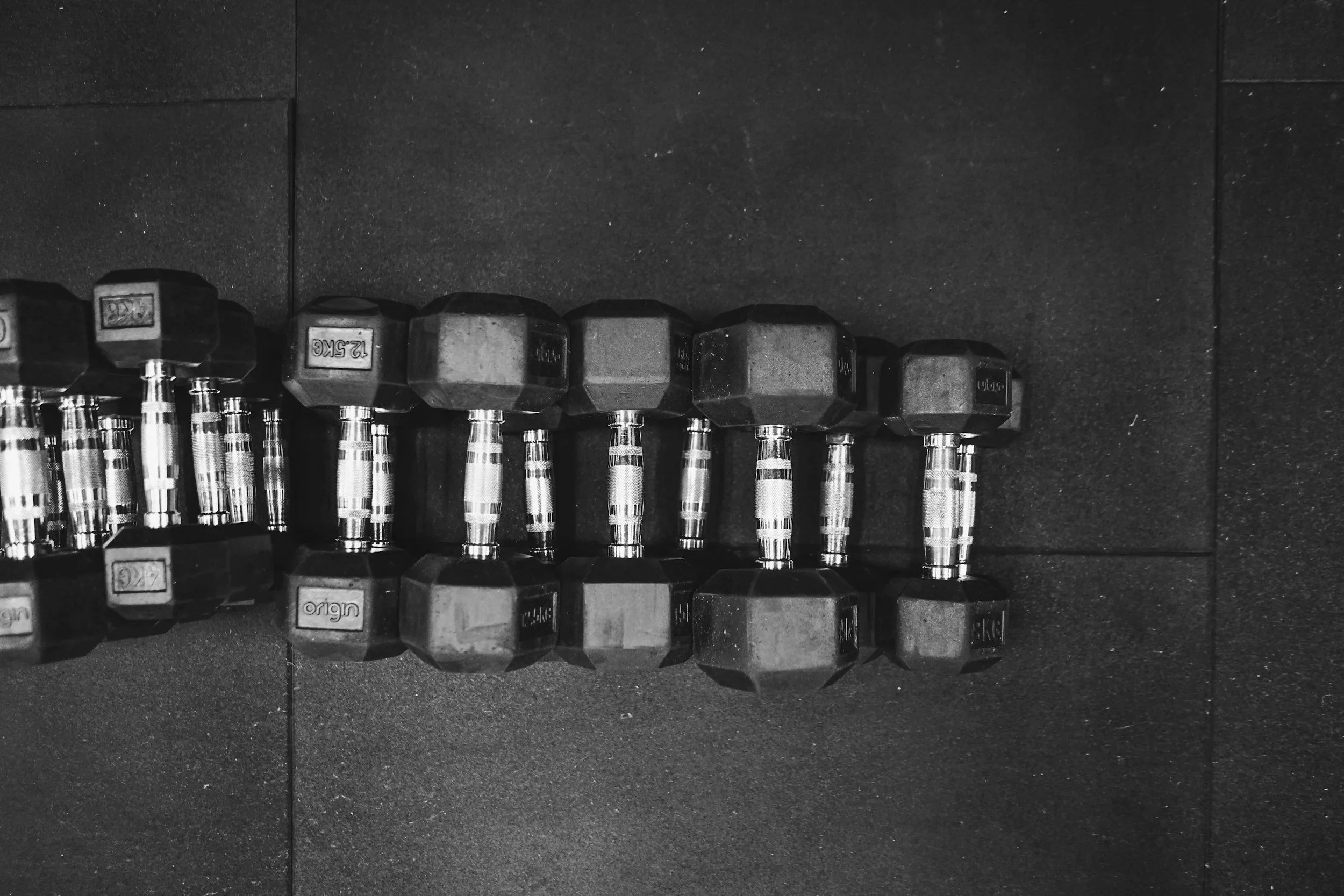 A row of hexagonal dumbbells with metallic handles on a dark gym floor.
