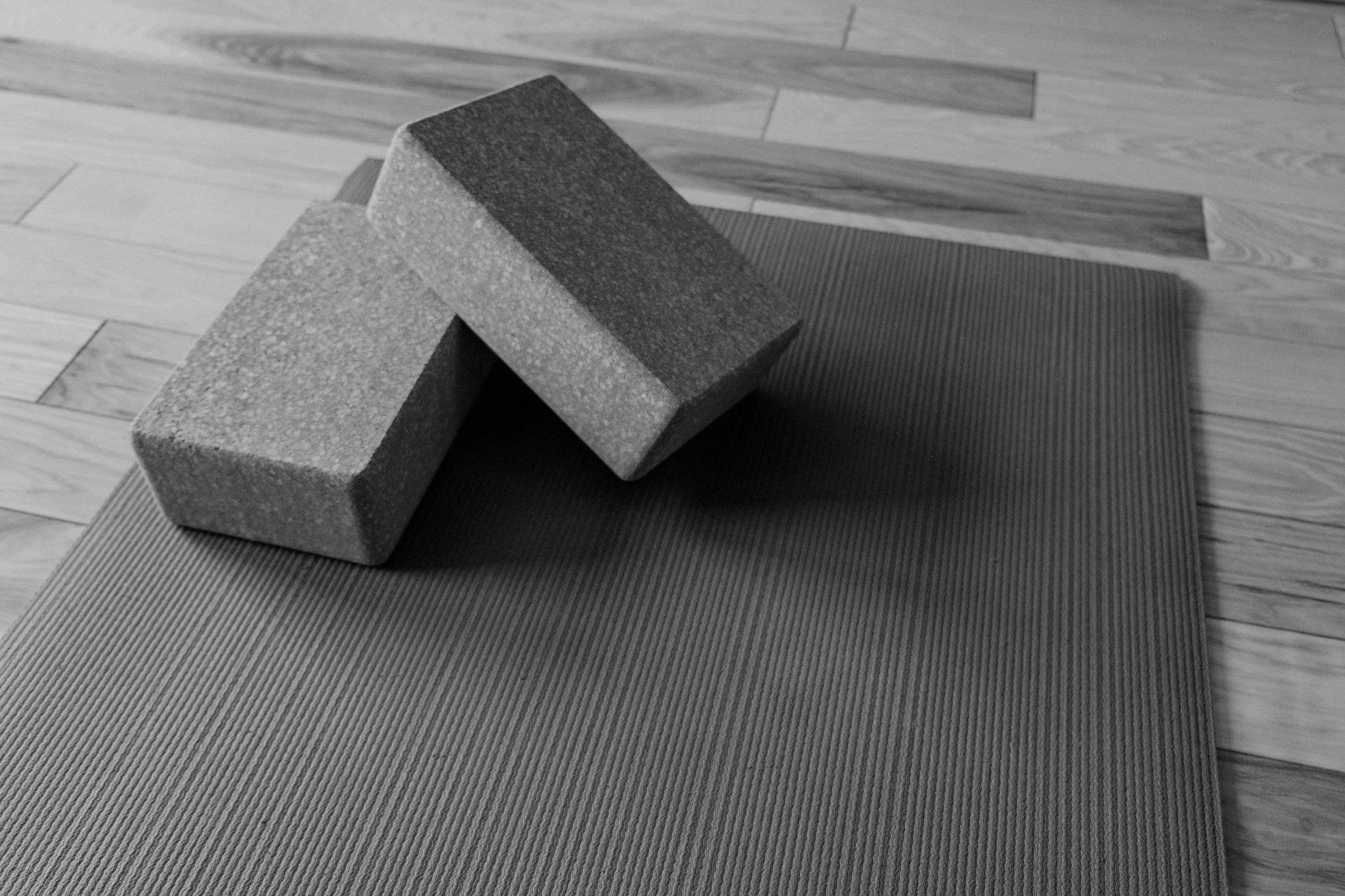 Two foam yoga blocks stacked on a textured yoga mat on a wooden floor.