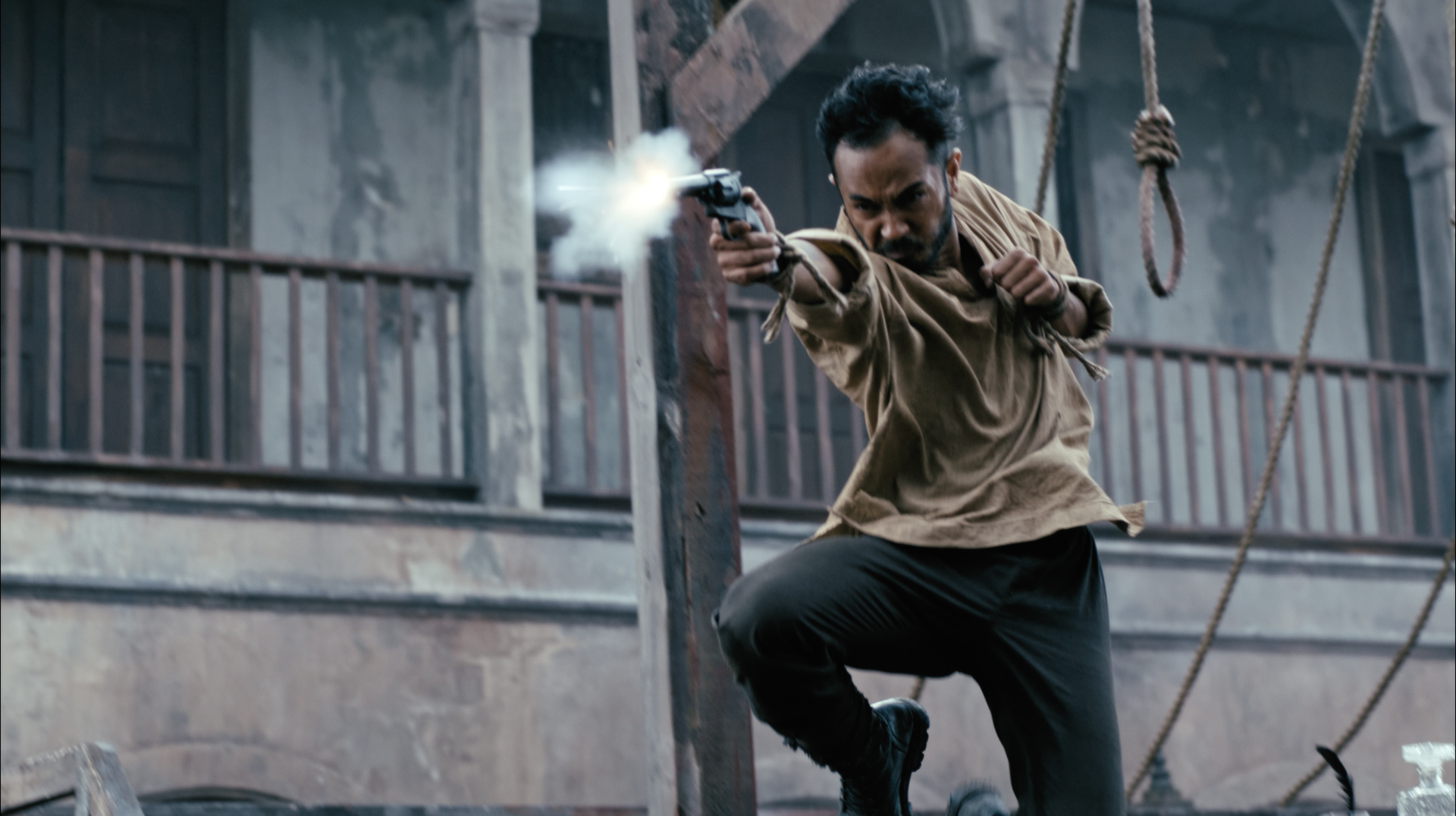Man aiming a pistol while crouching on a ship's deck with wooden railings and ropes.