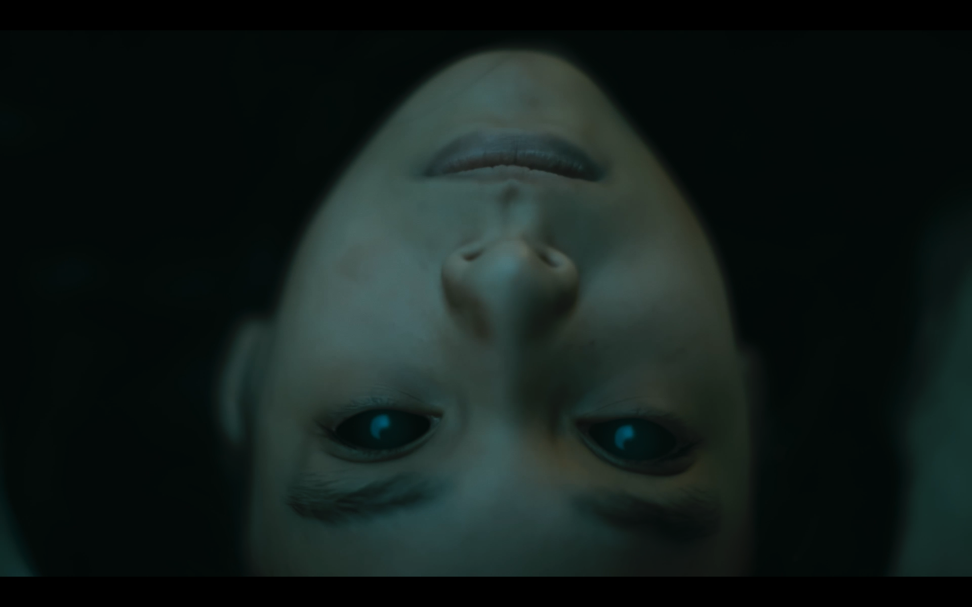 Upside-down close-up of a child's face with open eyes, lying in dark surroundings.