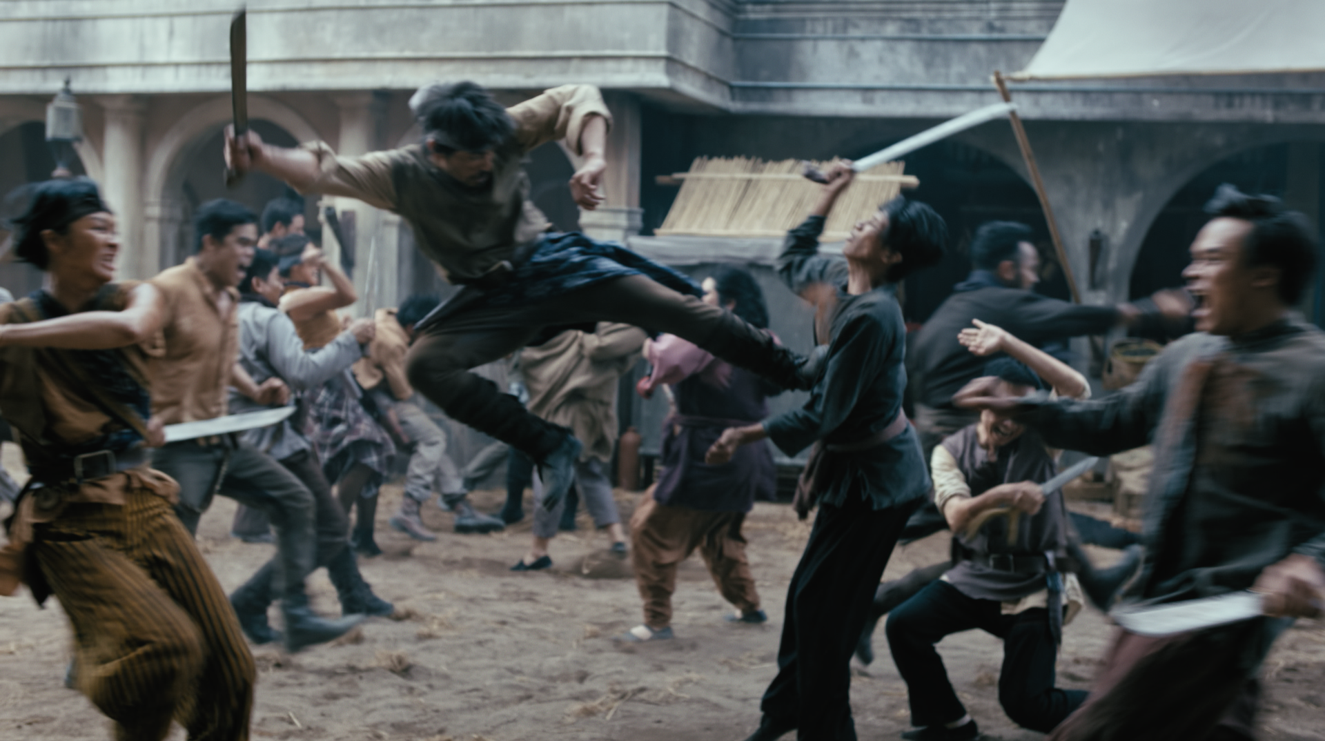 A fight scene with multiple people fighting with weapons in a historical or fantasy setting, with one man jumping into the fight mid-air.
