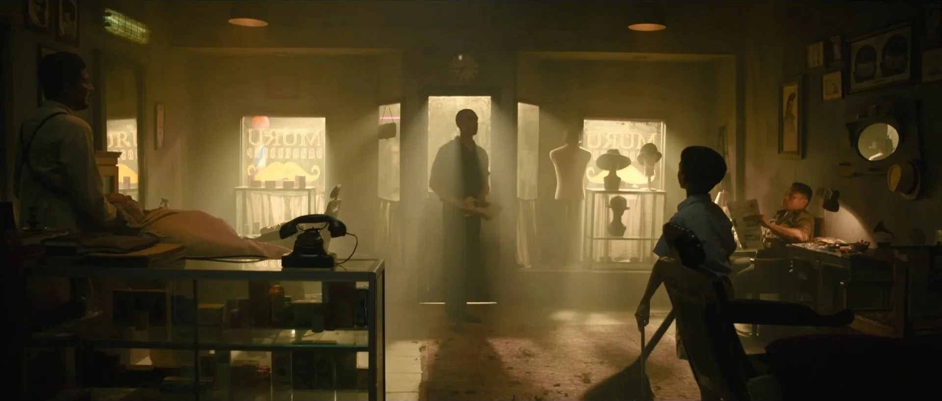 A dimly lit vintage shop with multiple people inside, sunlight streaming through the front windows, displaying mannequins, framed pictures, and various objects.