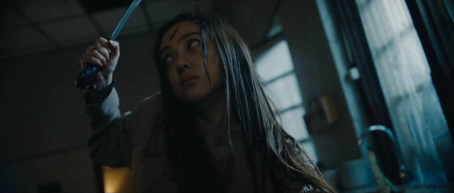 Woman with wet hair holding a knife over her head in a dimly lit room.