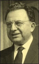 Black and white photograph of a man with glasses, wearing a suit and tie, smiling.