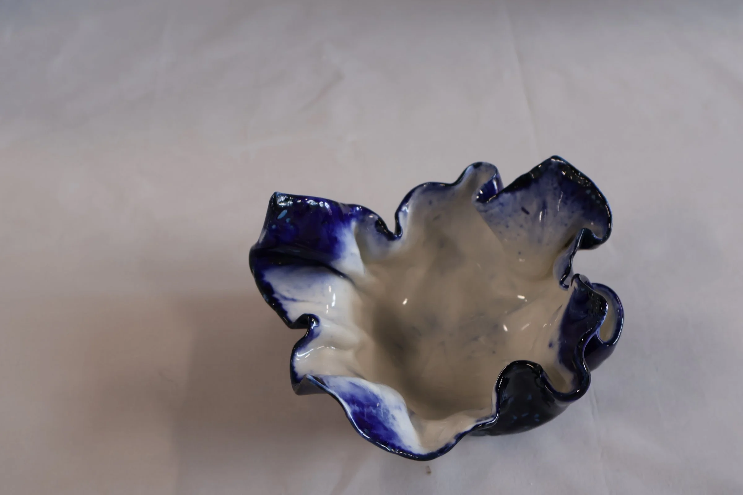 Ceramic bowl with ruffled edges, glazed in white and deep blue, placed on a plain surface.
