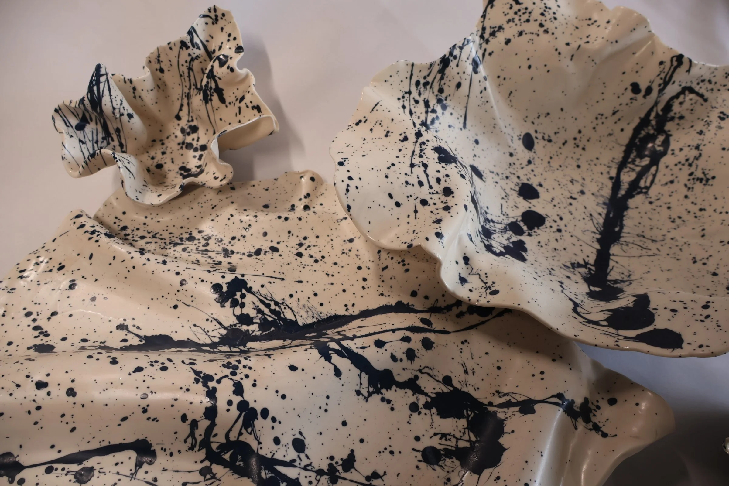 Cream-colored ceramic sculptures with black paint splatters and drips, resembling abstract art or decorative pieces.
