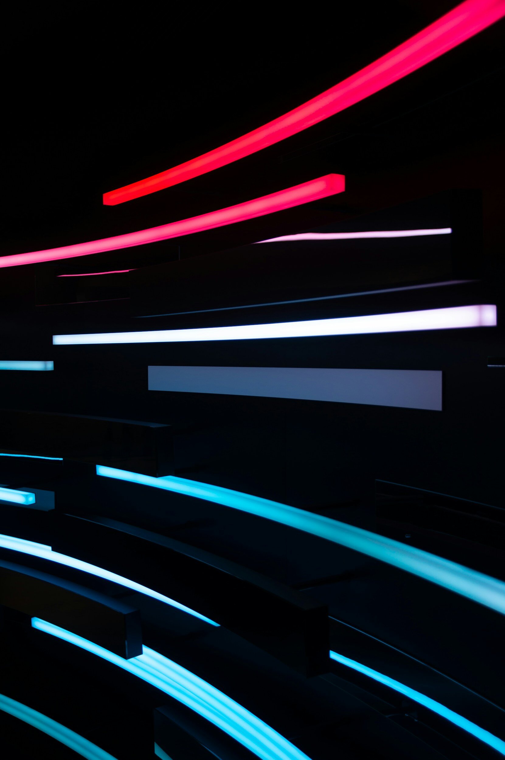 Colorful neon light streaks in red, pink, white, blue, and cyan on a dark background.