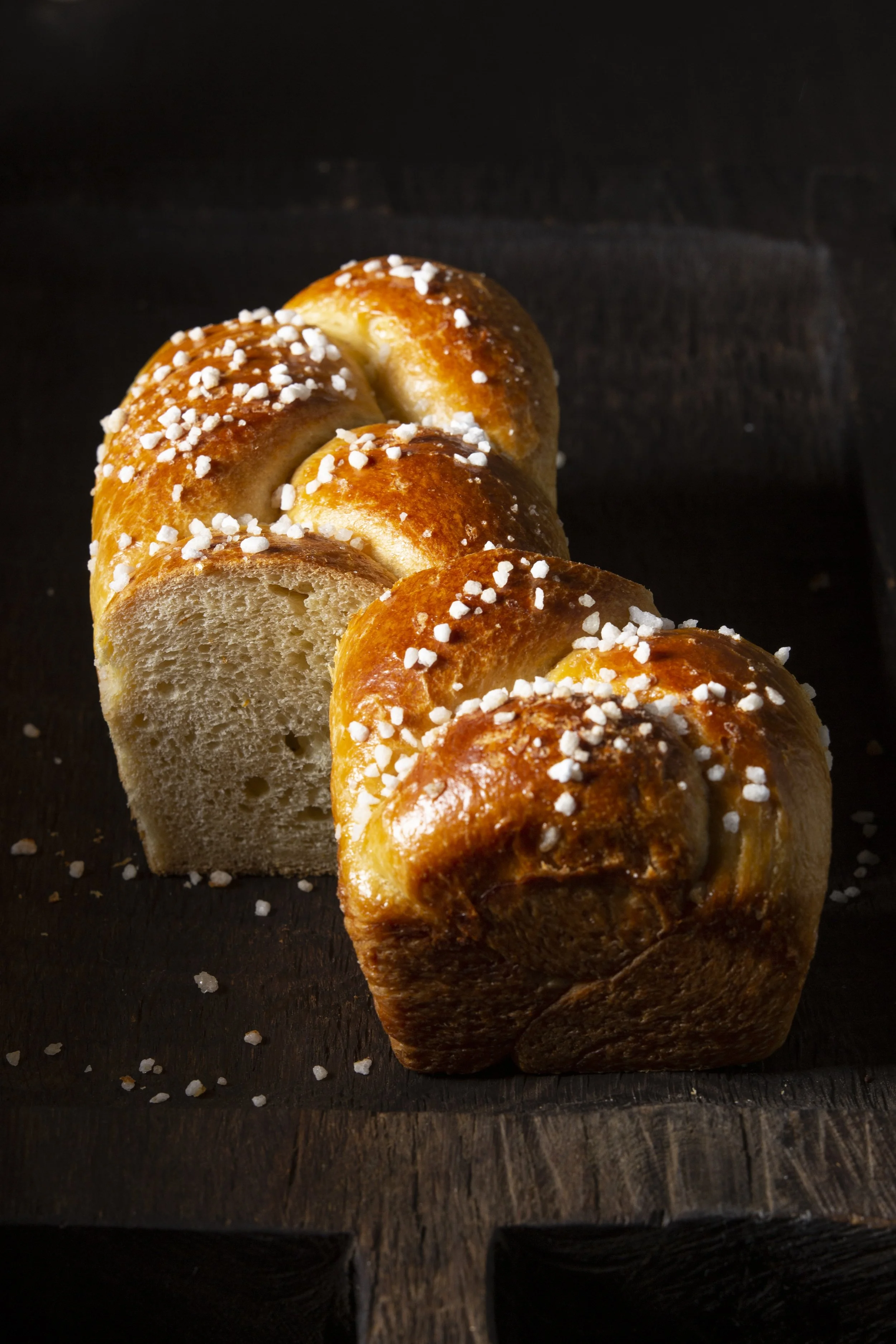 Goldenbraunes, frisch gebackenes Hefebrot mit Streusalz auf einem dunklen Holzbrett