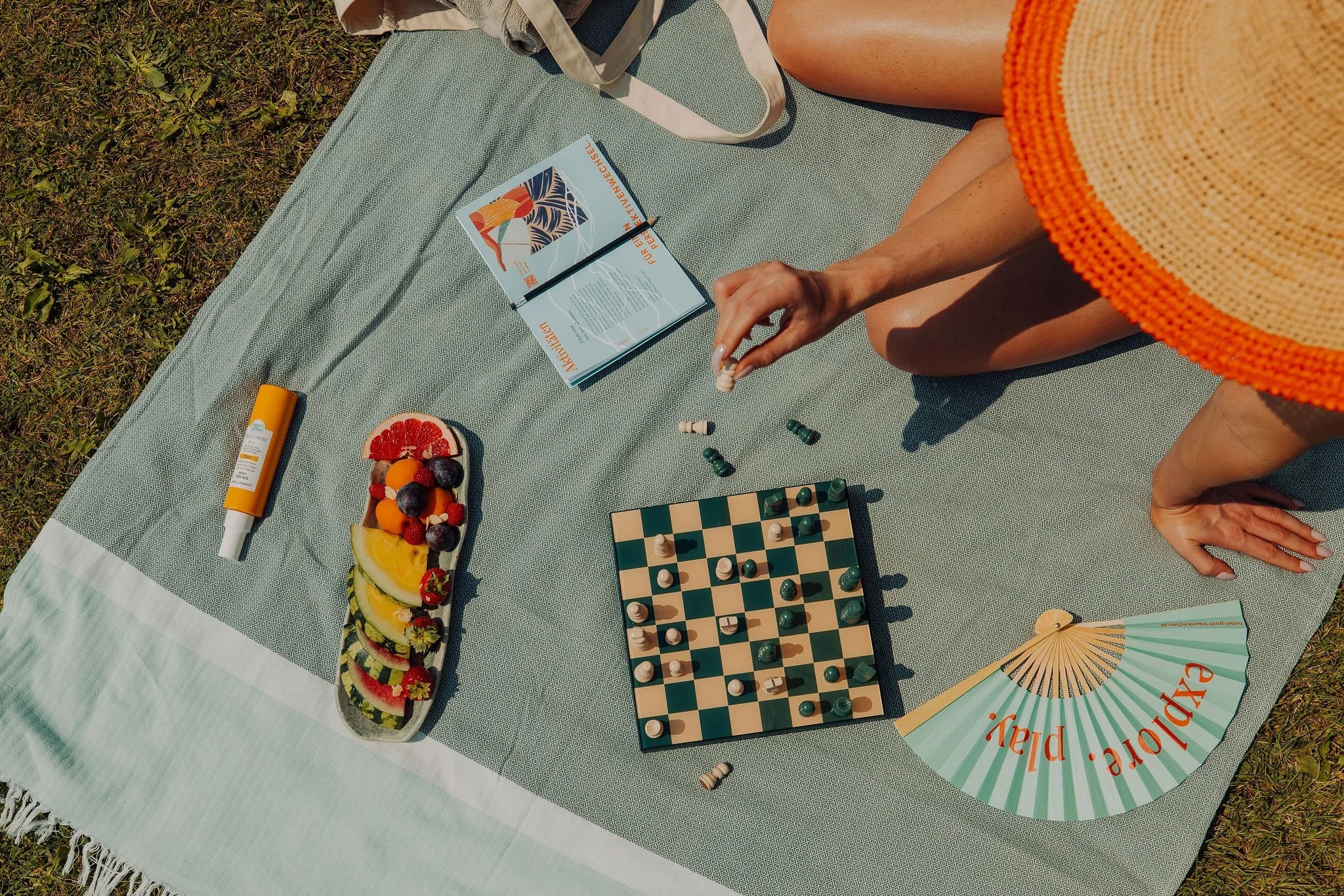 Eine Frau sitzt auch einem Handtuch auf der Wiese und spielt Schach für Post am See vom Studio für Branding Doppelpaula