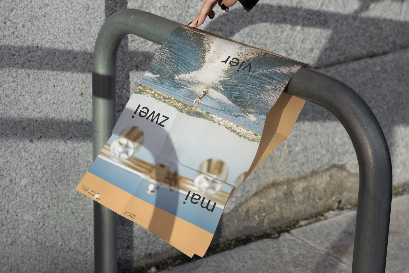 Das Poster „Mai, zwei, vier“ auf einem Fahrradständer, inszeniert vom Studio für Branding Doppelpaula. 