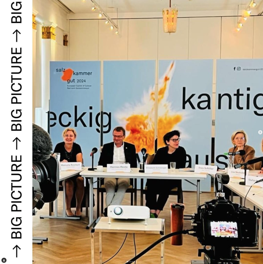 Vier Menschen sitzen an einem Tisch bei einer Konferenz. Hinter ihnen ist eine große Wand mit der Aufschrift 'salz kammer gut 2024' und einen Hintergrund mit einer Explosion. Es gibt Mikrofone und eine Kamera im Vordergrund.