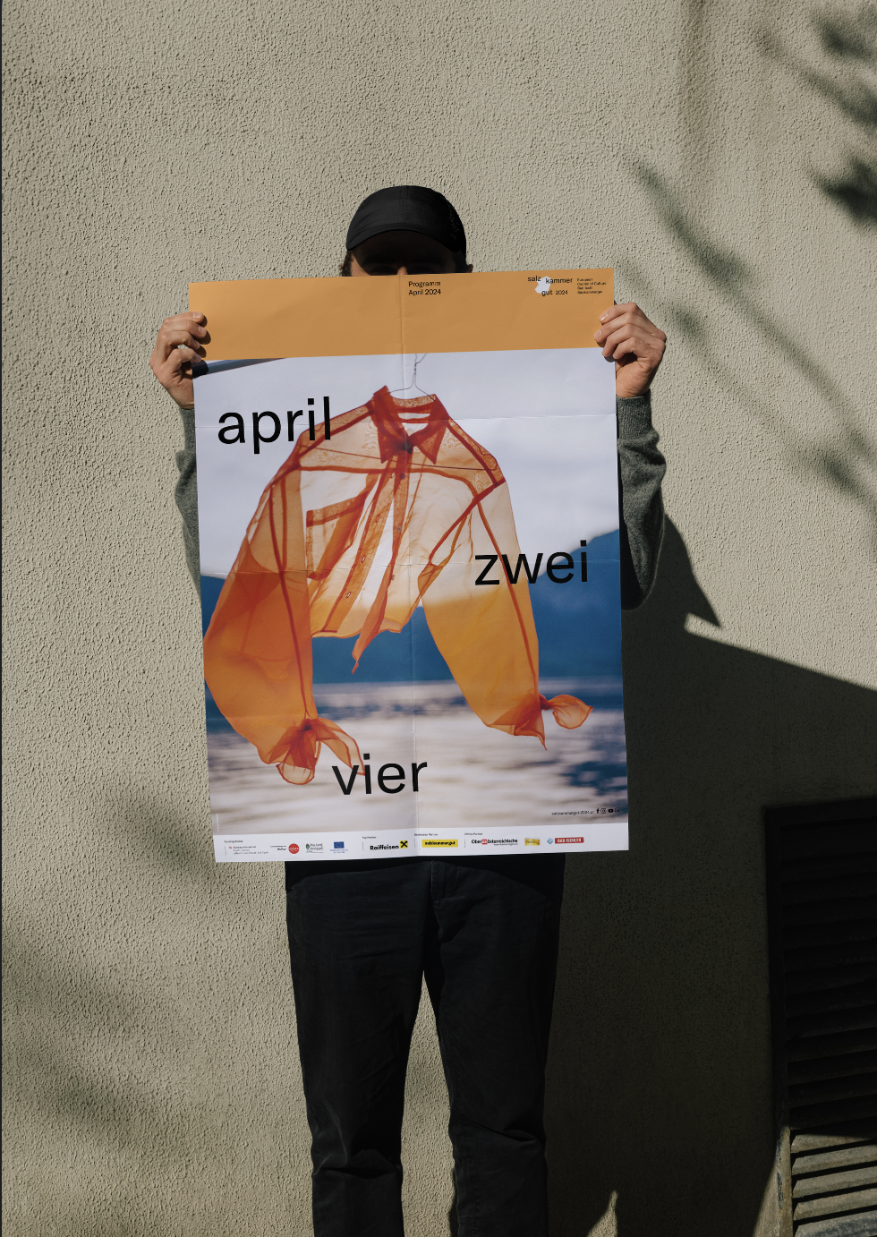 Eine Person hällt das Poster „April, zwei, vier“, inszeniert vom Studio für Branding Doppelpaula.