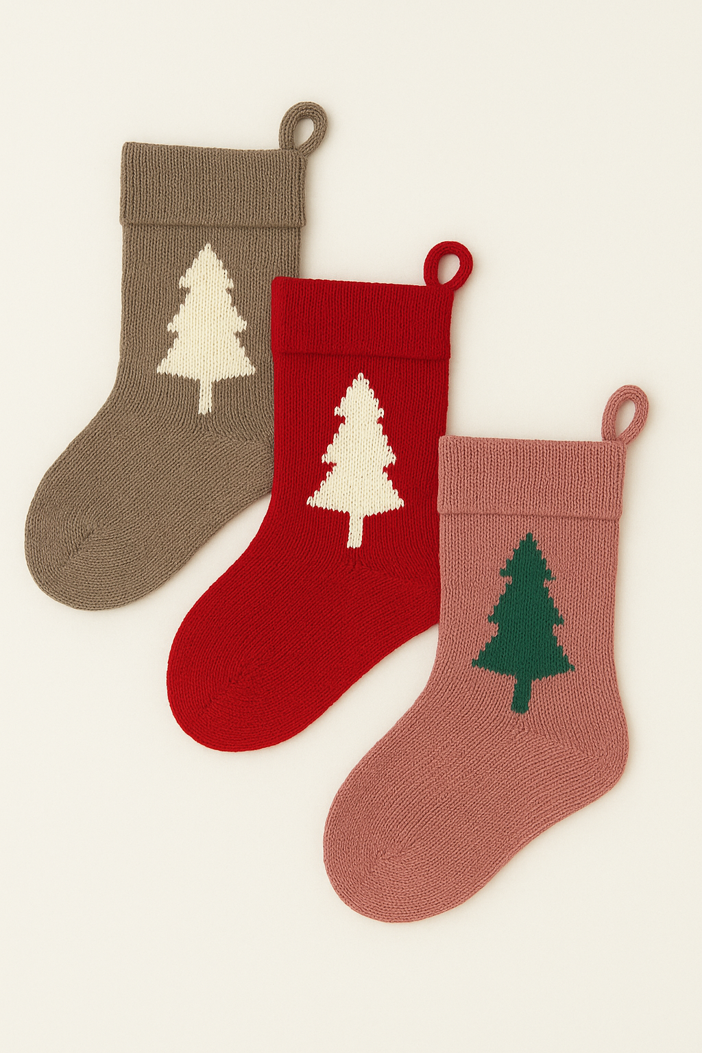 Flat lay of three Loré Loré Christmas stockings layered on an angle, featuring Christmas tree motifs in knitted natural fibres.