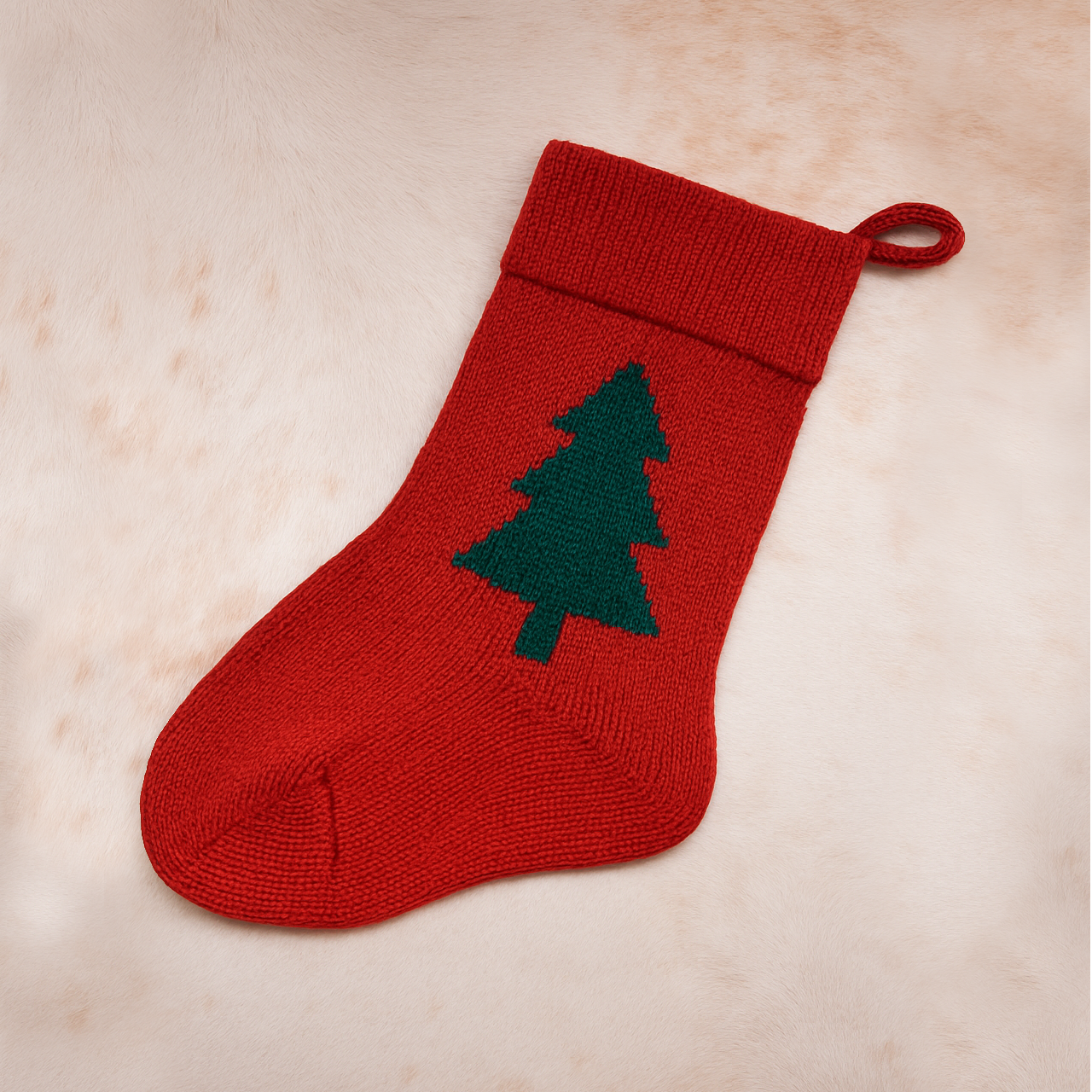 A machine-knitted Christmas stocking in red with an emerald green tree motif, displayed on a soft neutral background. Handmade by Loré Loré, showcasing christmas stocking workshop product.