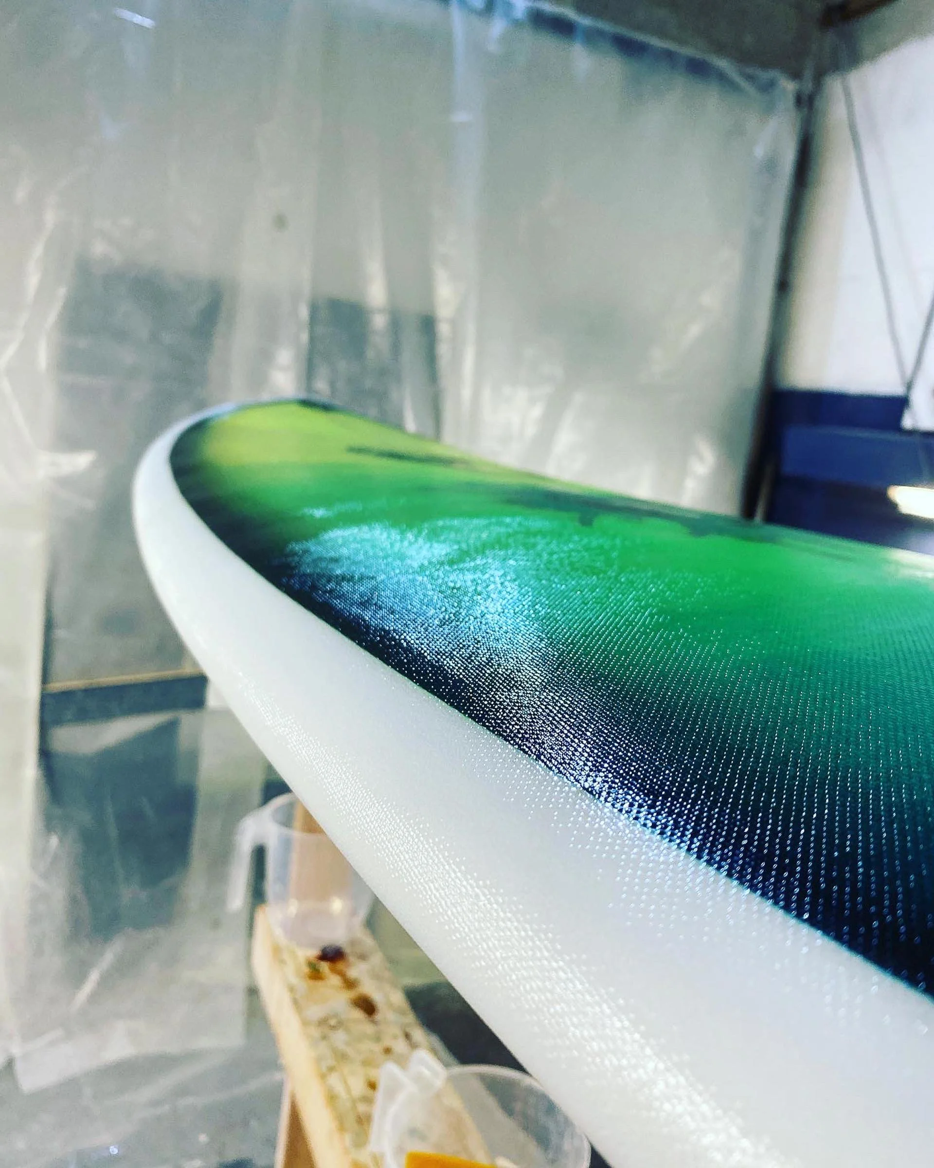 Close-up photo of a surfboard with a green and black design, resting on a stand in a workshop or storage area.