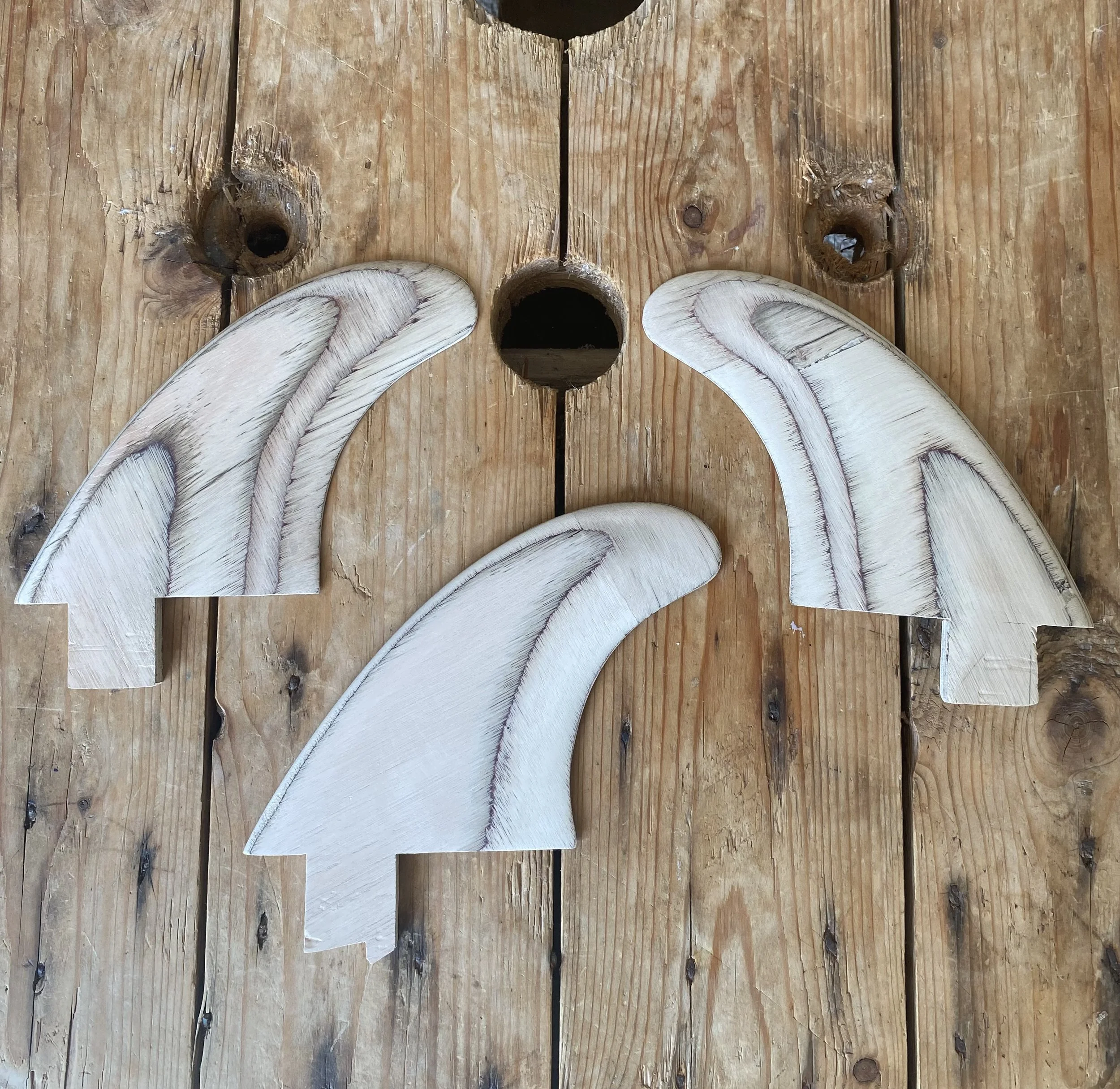 Three wooden cutouts of whale fins on a rustic wooden surface.