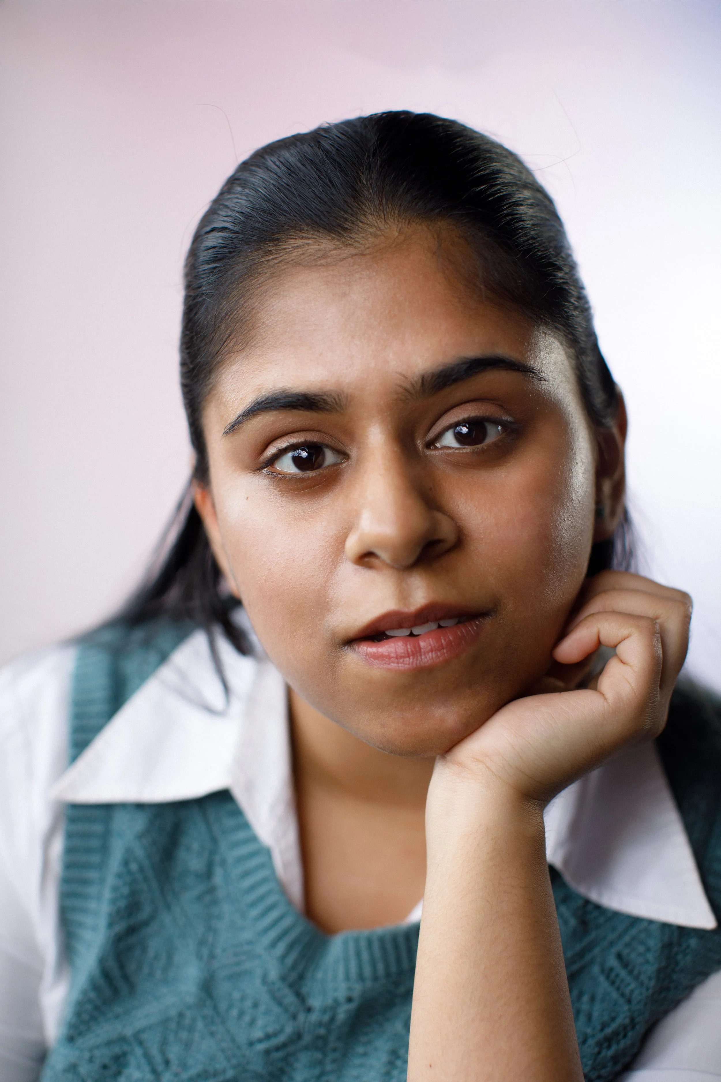 A woman sitting on stairs with a smile, wearing a snake print dress, in front of a dark wall with a window showing a blue sky and a yellow light.