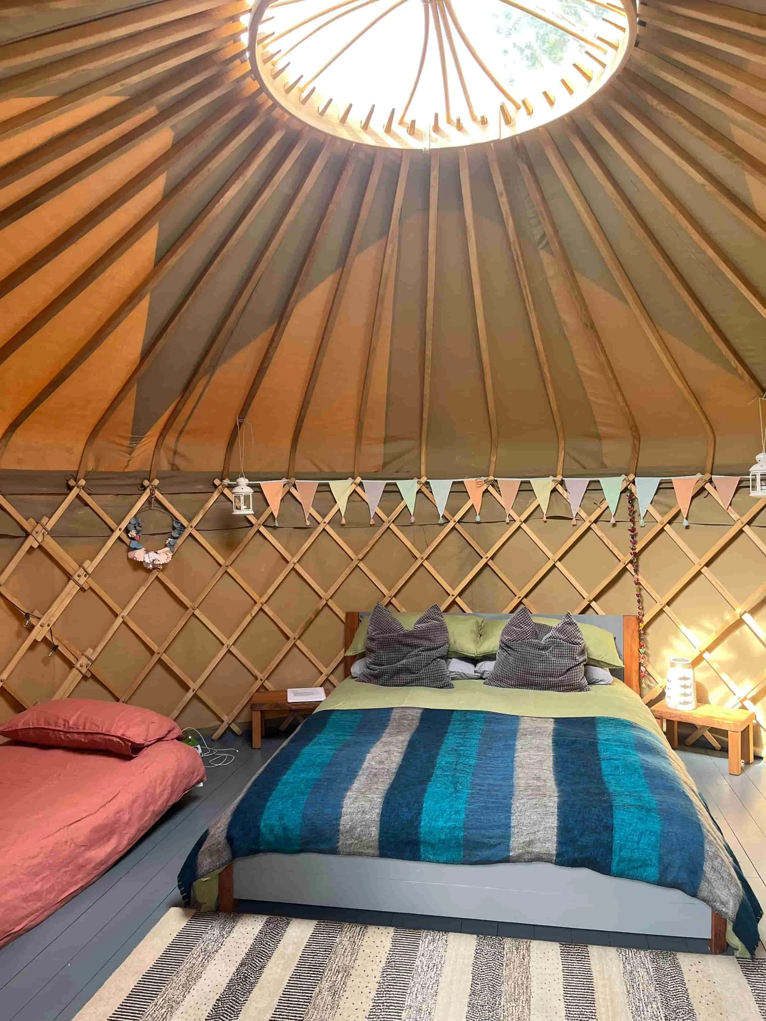 Yurt interior showing beautiful crown and star cover in ceiling, king sized bed and wool blankets and cushions