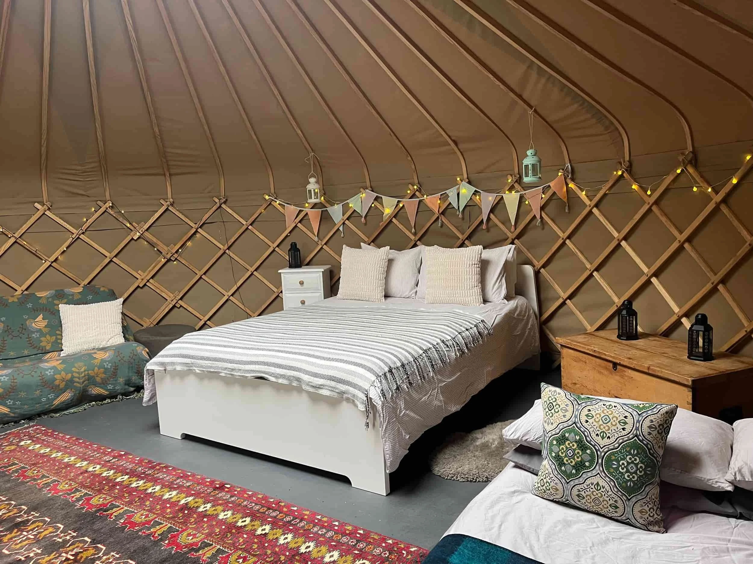 Yurt interior with double bed, fairy lights, bunting, kilim rug and wood-framed lattice walls, Botswicky