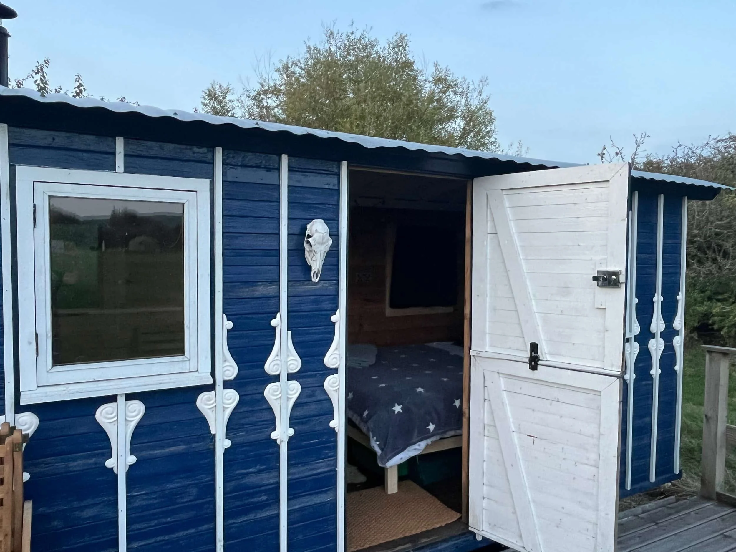 Rustic blue shepherd's hut with open stable door, star-print bedding visible inside, Botswicky Wiltshire