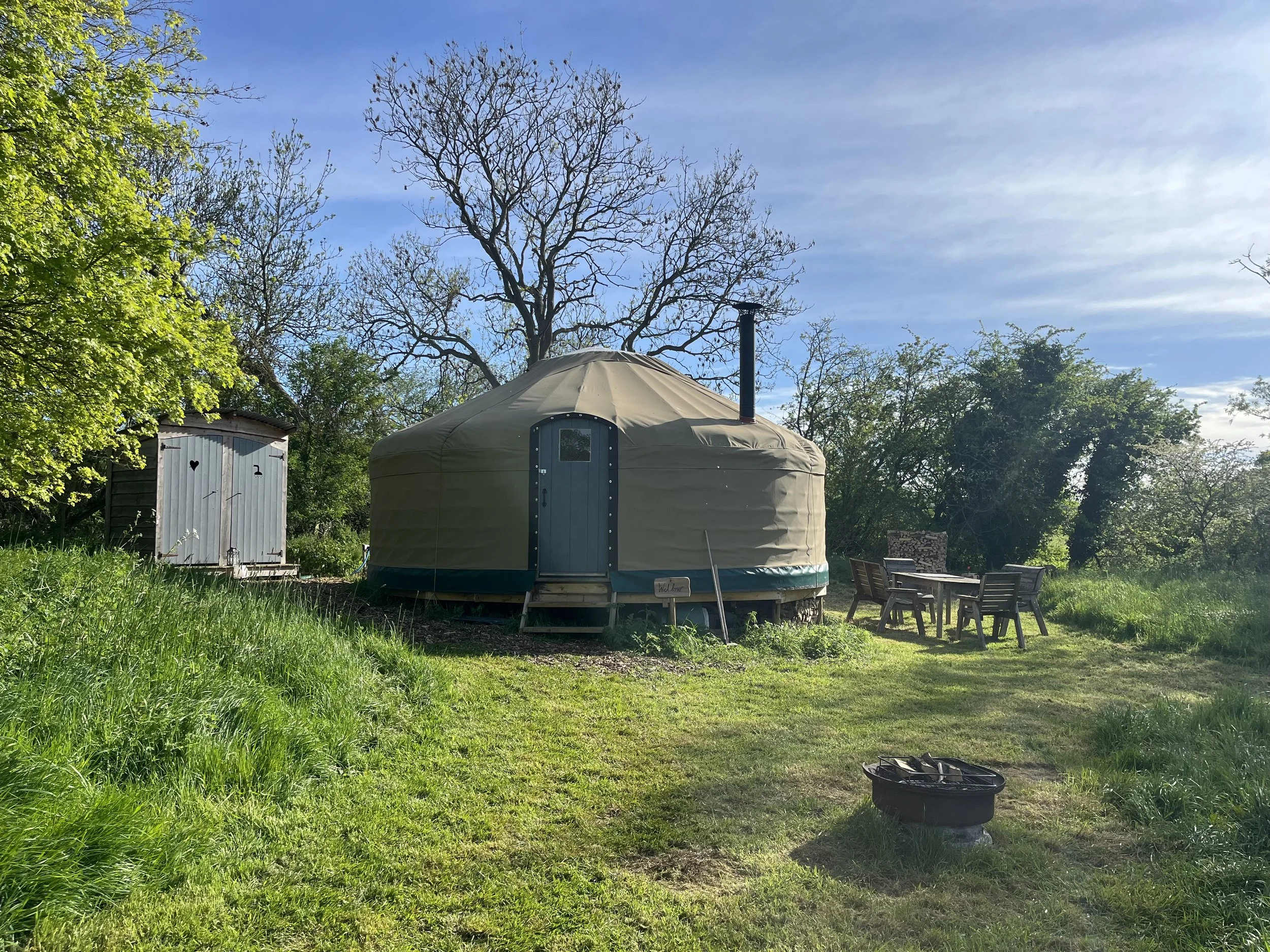 A beautifully hand-built steam bent yurt surrounded by trees and lush green grass at Botswicky Copse