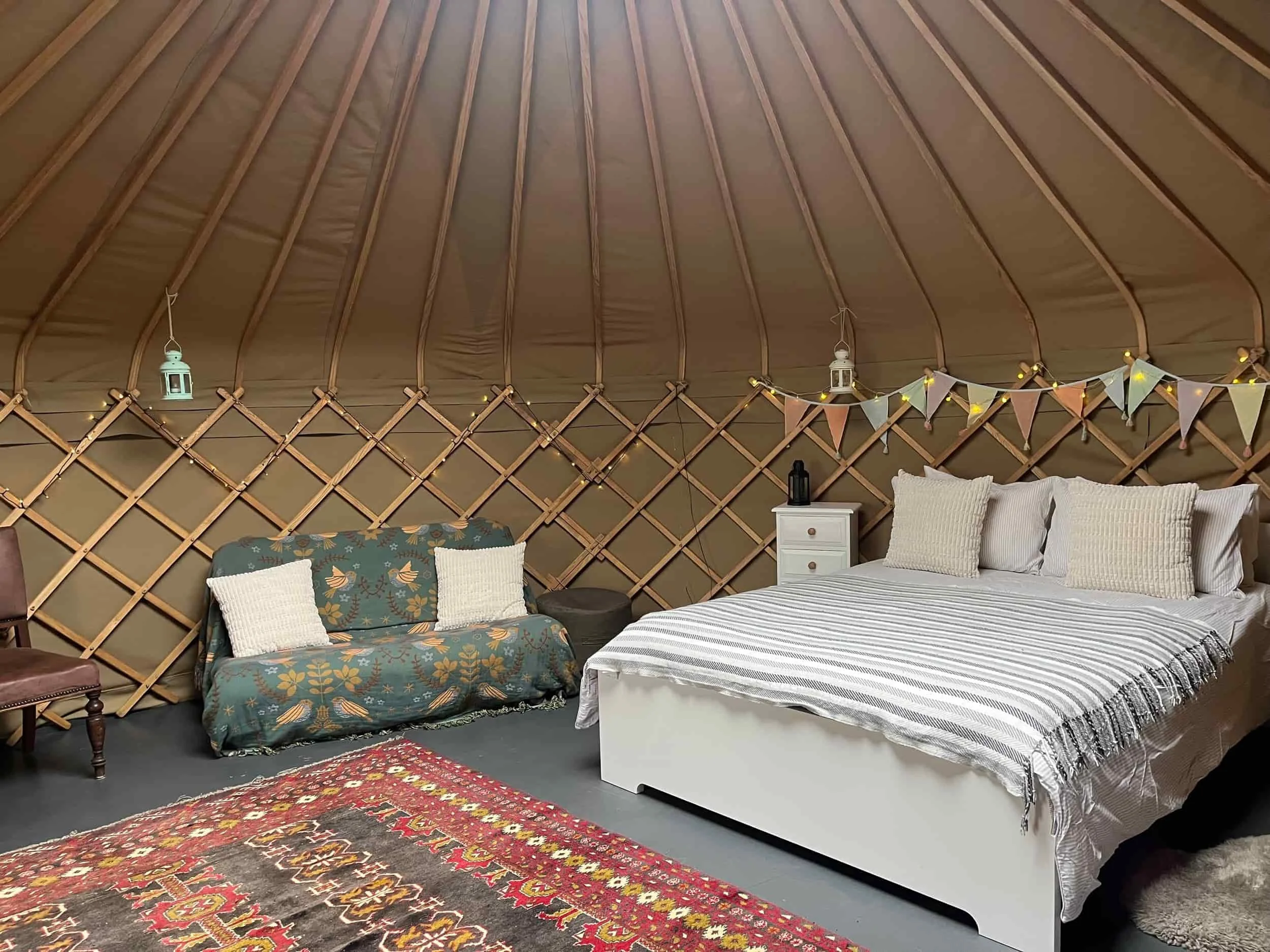 Yurt interior with natural decor, a king sized bed and sofa with decorative cushions and wooden furniture