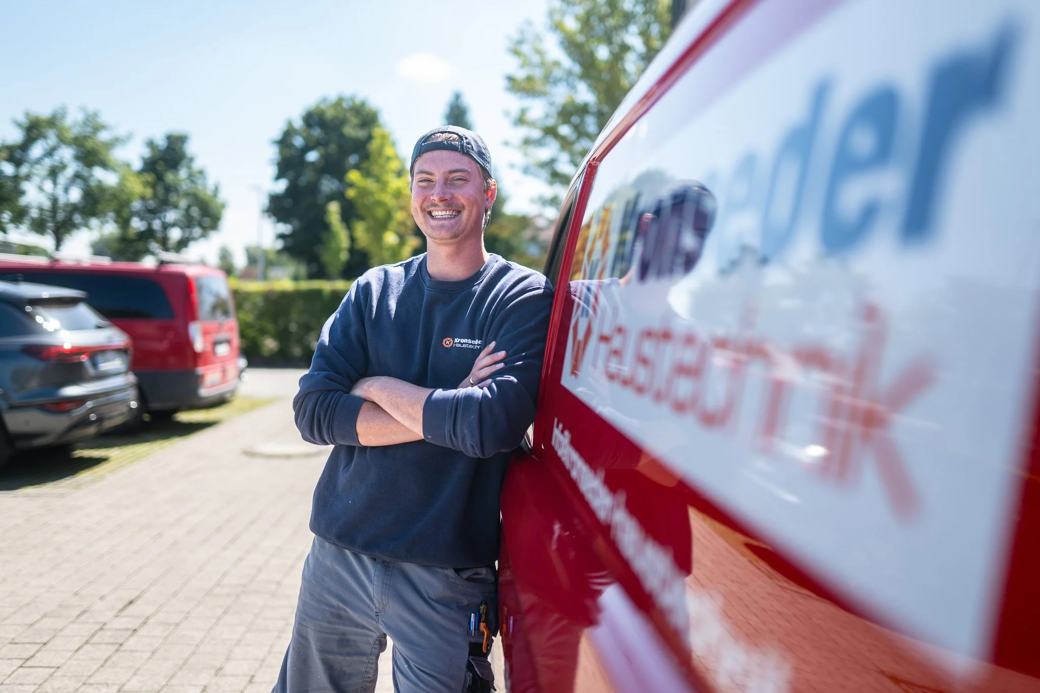 Lächelnder Mann, der neben einem roten Feuerwehrfahrzeug steht, bei sonnigem Wetter im Freien.