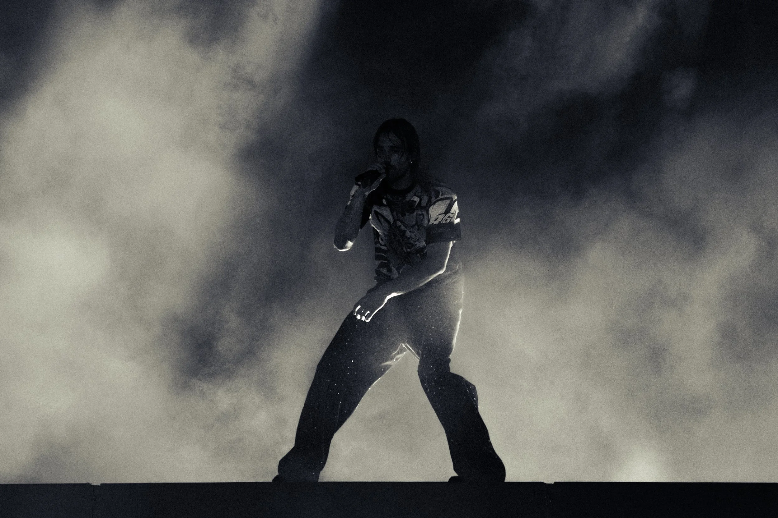 Ein Sänger auf einer dunklen Bühne, umgeben von Rauch, beim Auftritt in der Nacht.