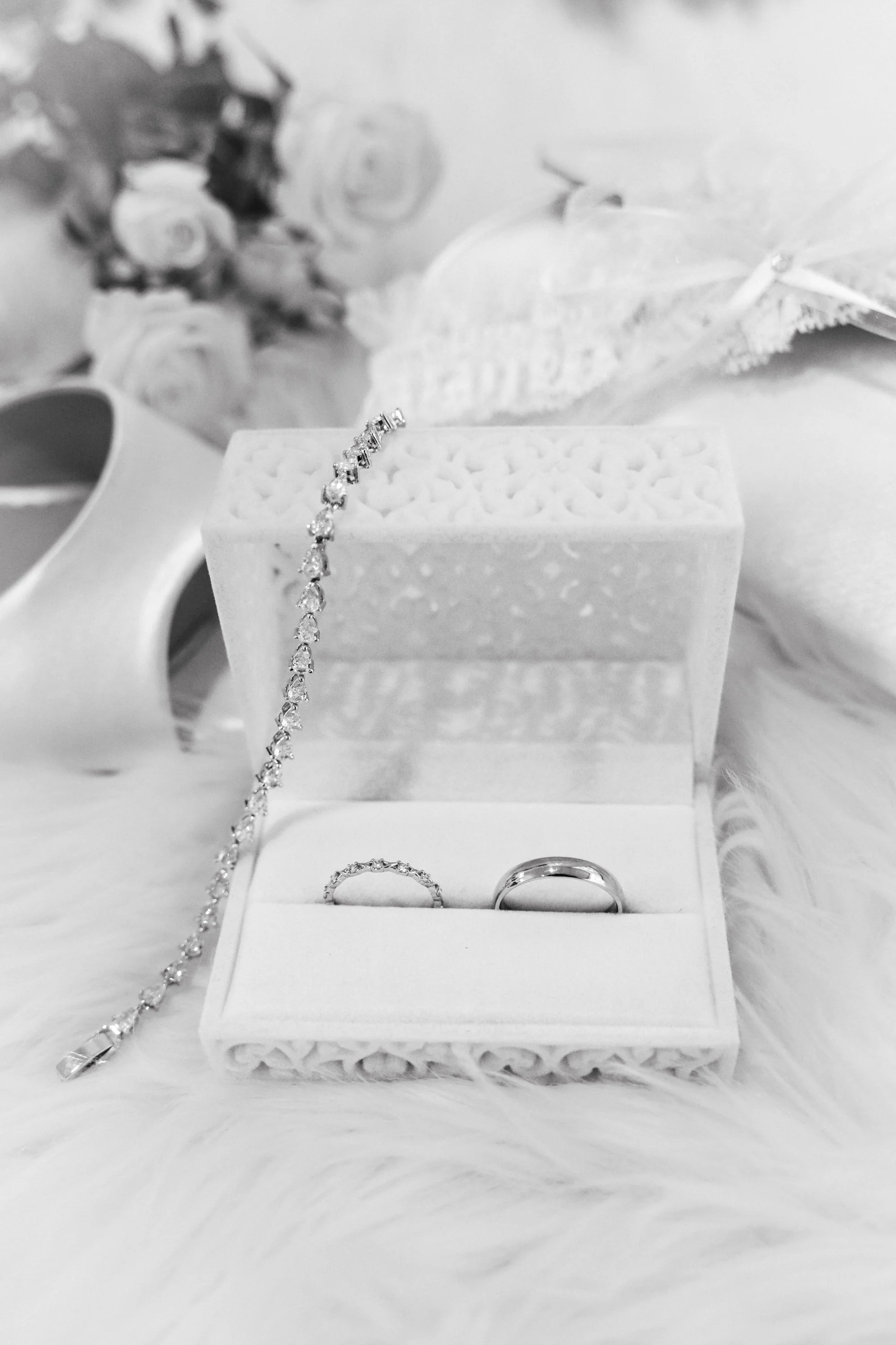 Wedding rings and jewelry in an elegant box, with roses, a candle, and decorative leaves in the background.