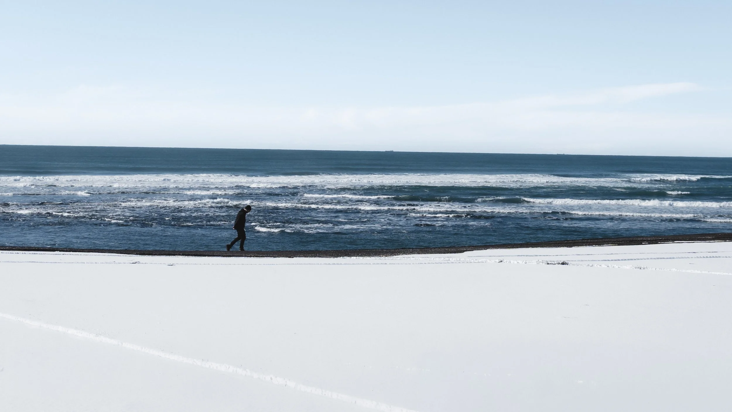 A person walking along a snowy beach with the ocean in the background.