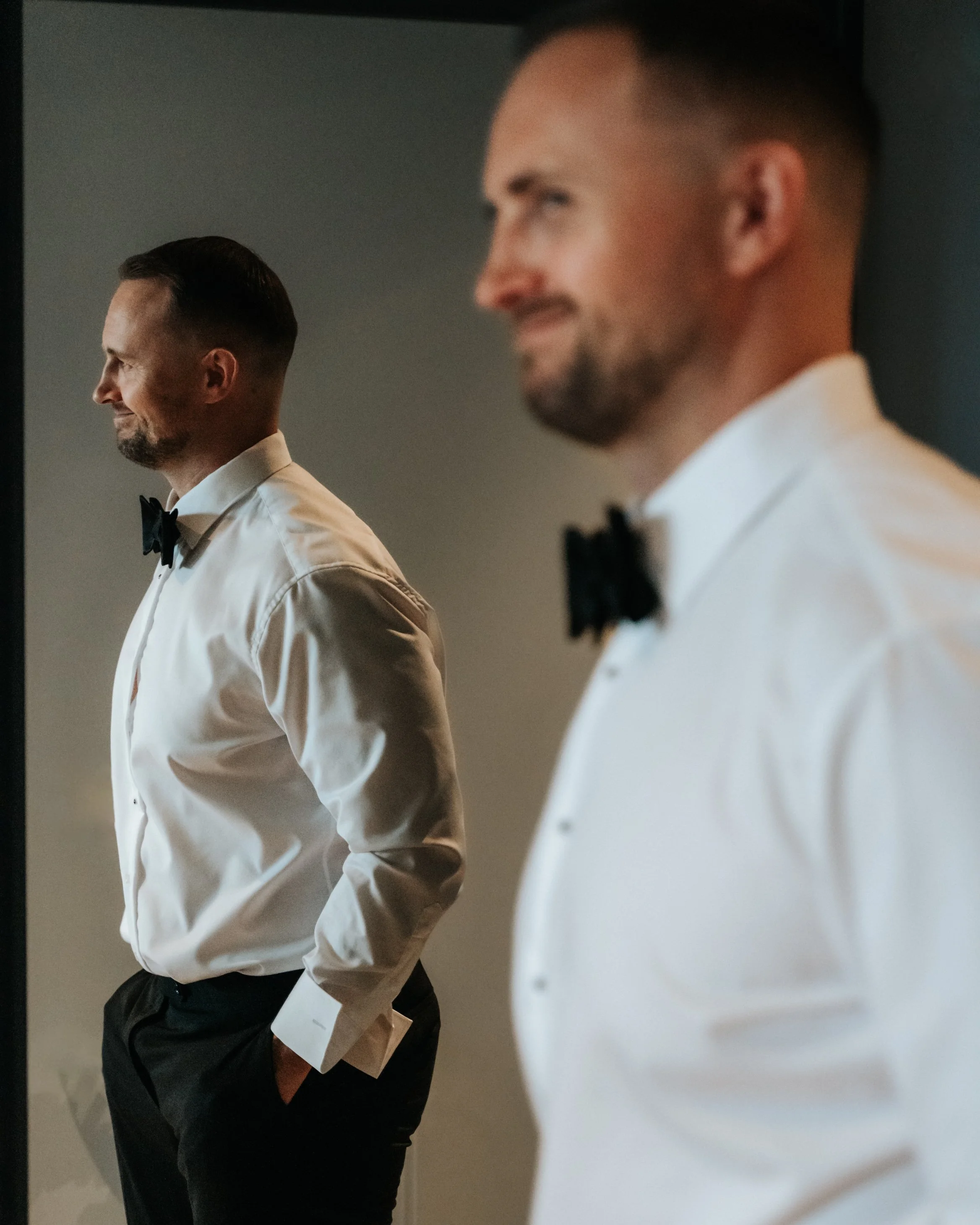Man in white shirt and bow-tie reflected in a mirror.
