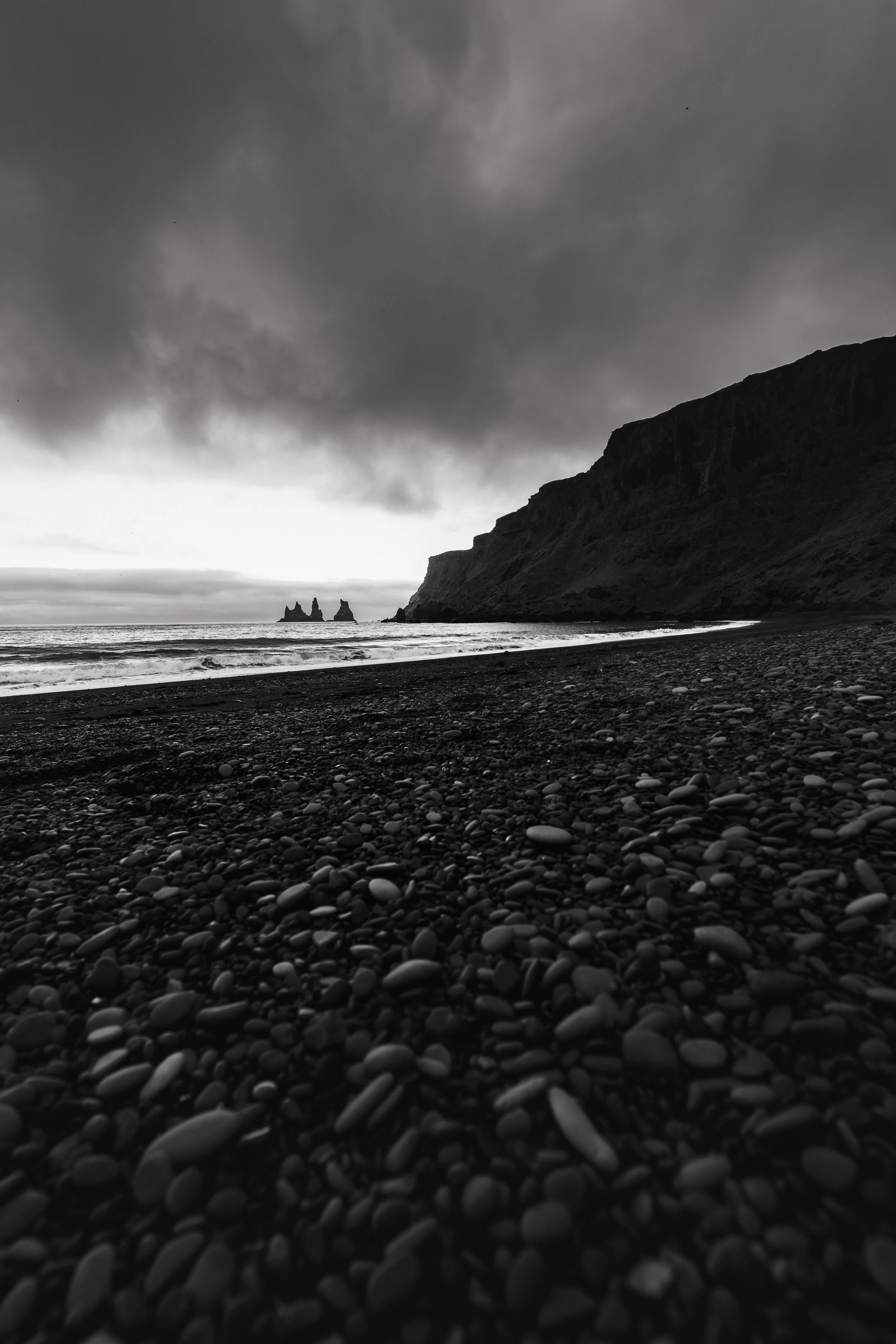 A quiet stretch of black sand near Vík í Mýrdal, where the land softens into the sea. In the distance, the Reynisdrangar rise through the haze as the horizon fades and everything holds still.