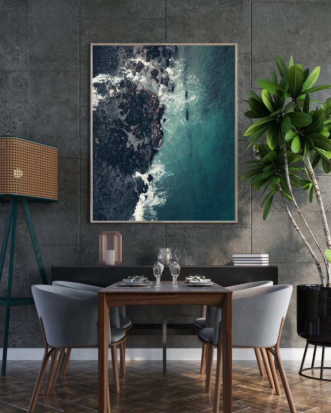 A modern dining room with a large wall art photograph of crashing ocean waves and rocks, a wooden table with four gray chairs, and potted green plants, including a tall rubber plant.