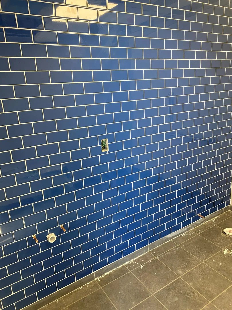 Wall with blue subway tiles and gray floor tiles, with plumbing fixtures visible.