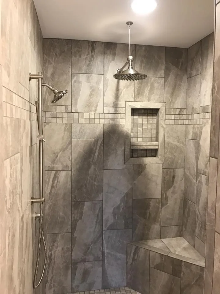 Modern tiled shower with rain showerhead, hand-held shower, built-in bench, and recessed shelves.