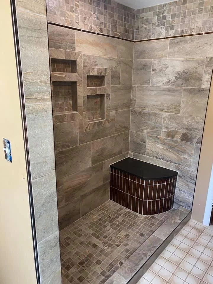 Modern tiled shower with built-in niches and a corner bench. The walls feature a mix of large rectangular tiles and small square tiles.