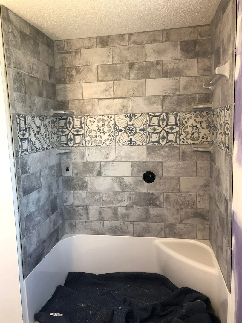 Bathroom wall with gray and patterned tiles above a bathtub