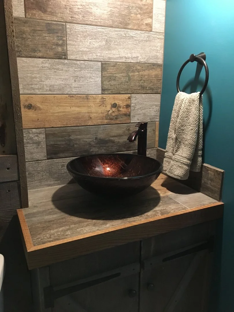 Rustic bathroom vanity with a stone bowl sink and dark faucet, set against a wooden wall. A hand towel hangs on a black ring on the adjacent aqua wall.