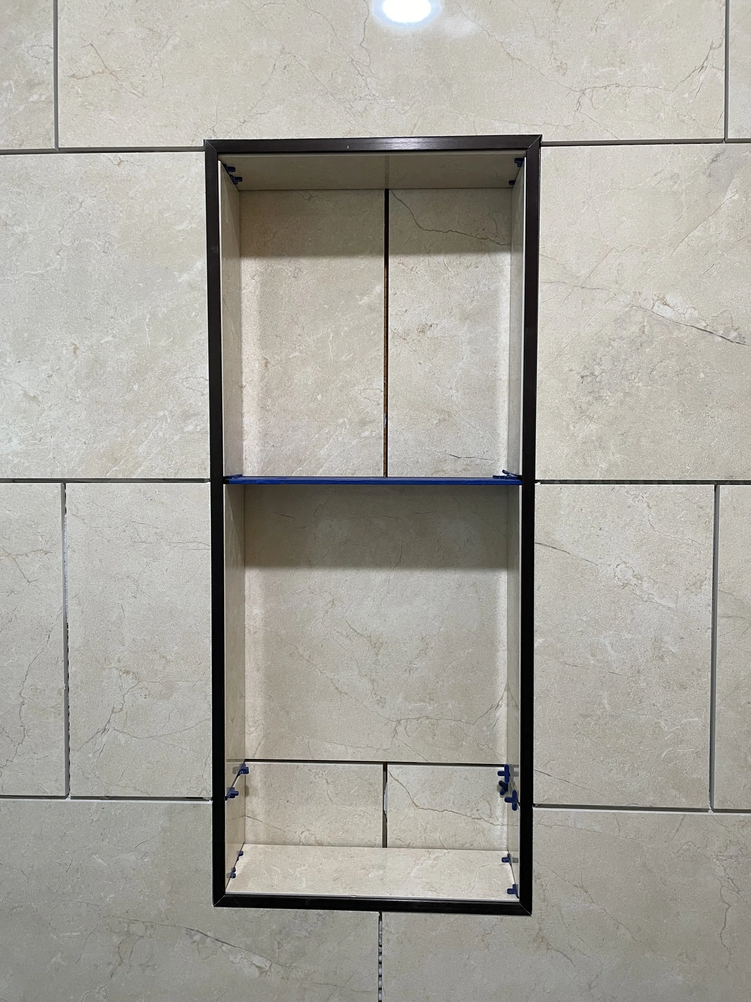 Empty recessed black metal shelf set into a beige tiled wall.