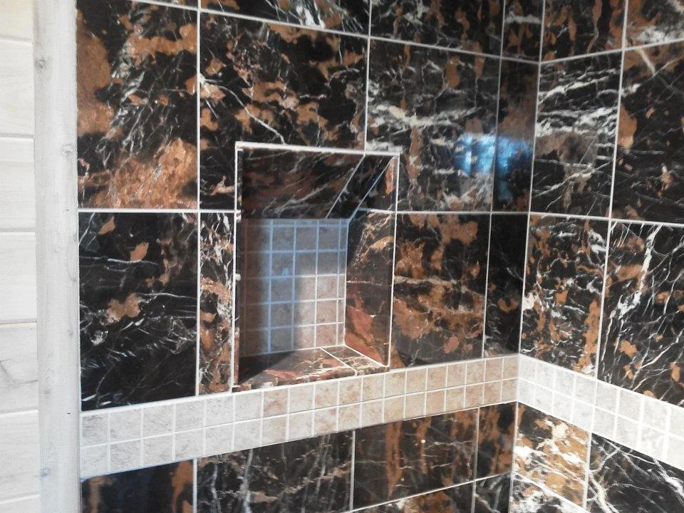 Bathroom wall with black and brown marble tiles, featuring a recessed shelf lined with smaller contrasting tiles.