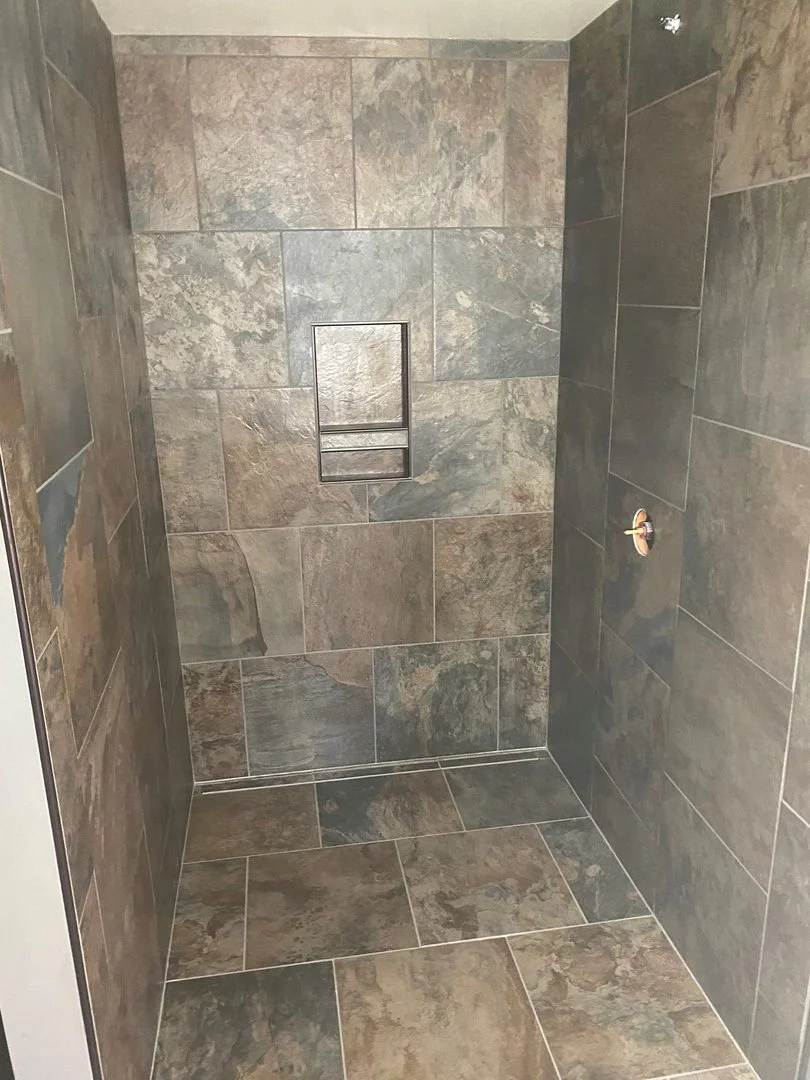 A walk-in shower with brown and gray stone tiles, featuring a built-in shelf.