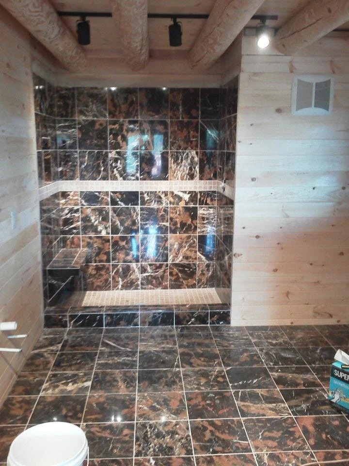 Bathroom with marble tile floor and shower, wooden walls, and exposed beam ceiling.