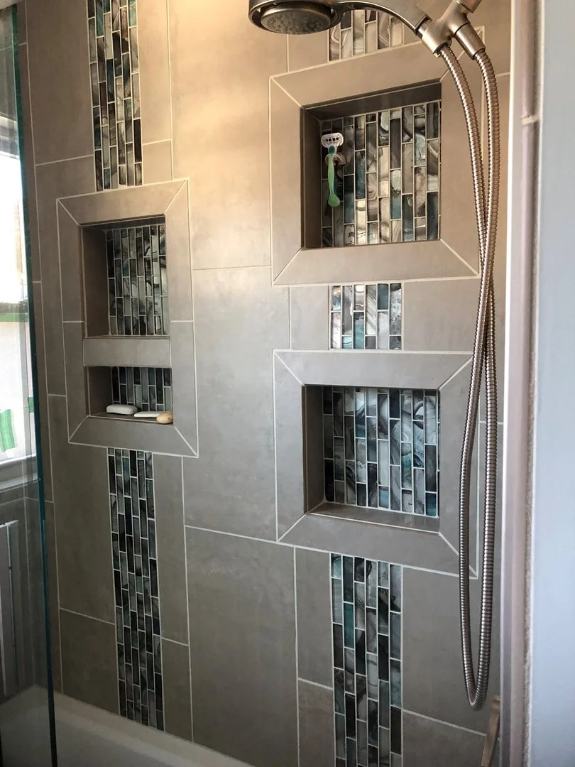 Shower area with mosaic tile accents and built-in niches, featuring a showerhead and handheld spray.