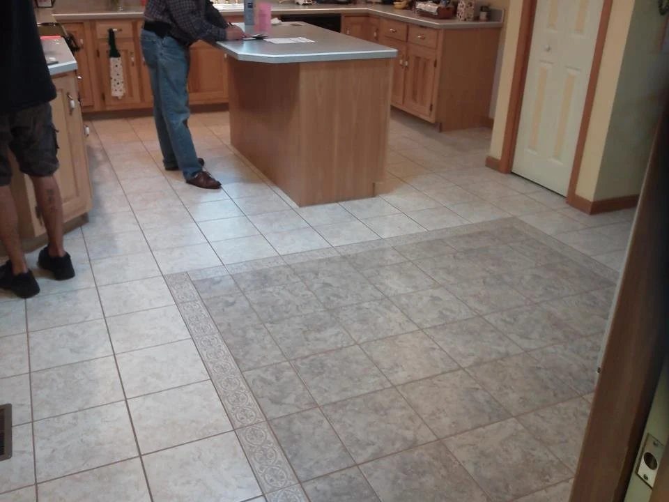 Kitchen with tiled floor, wooden cabinets, and a man standing by the island.
