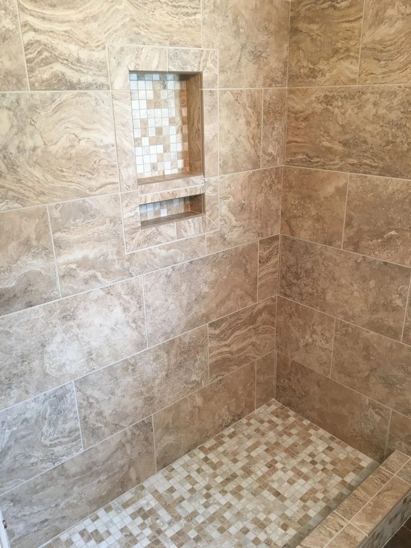 Tile shower with beige and brown marble-like wall tiles and small square mosaic tiles in the niche and floor.