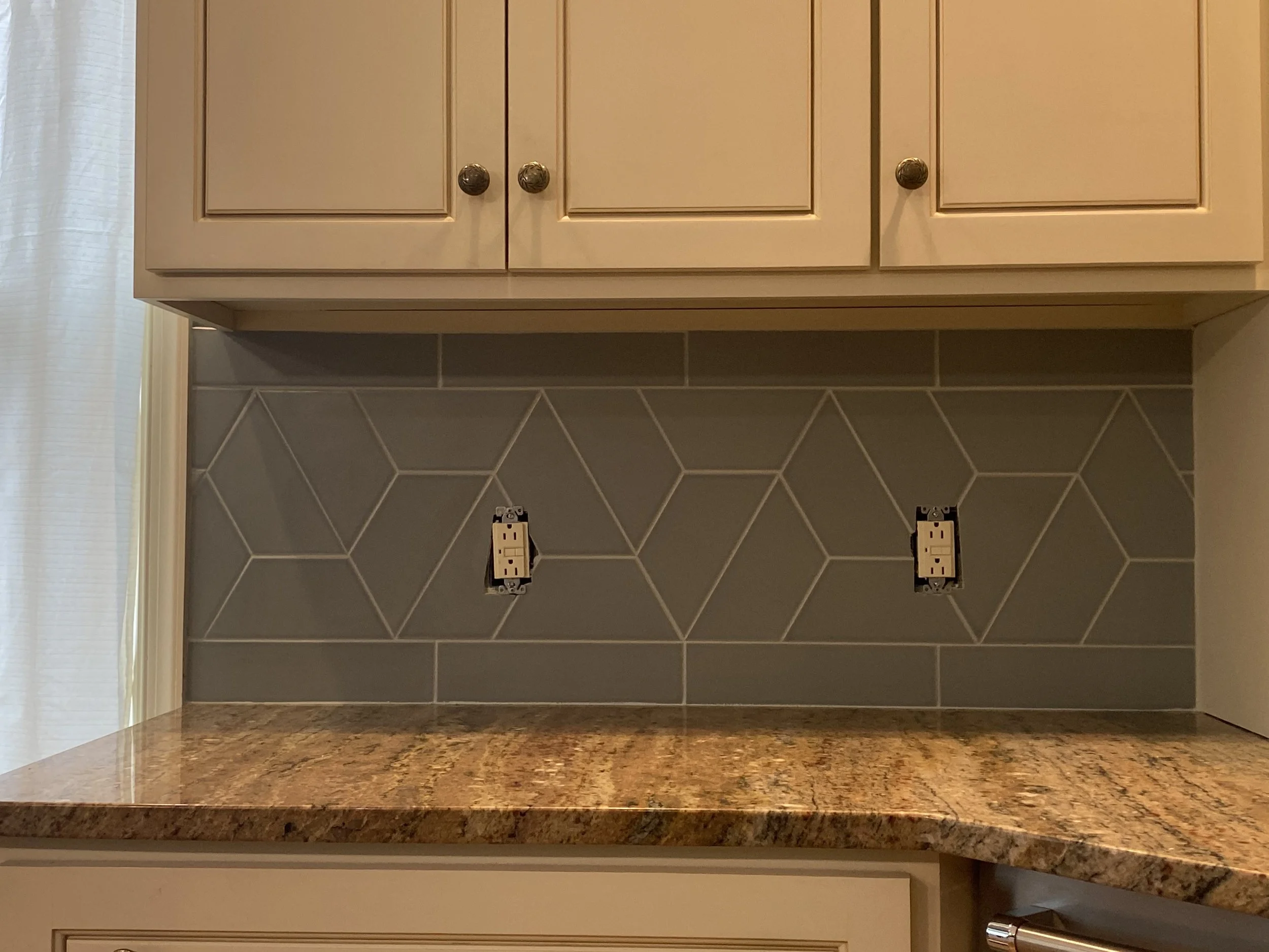 Kitchen countertop with geometric tile backsplash and beige cabinets above.