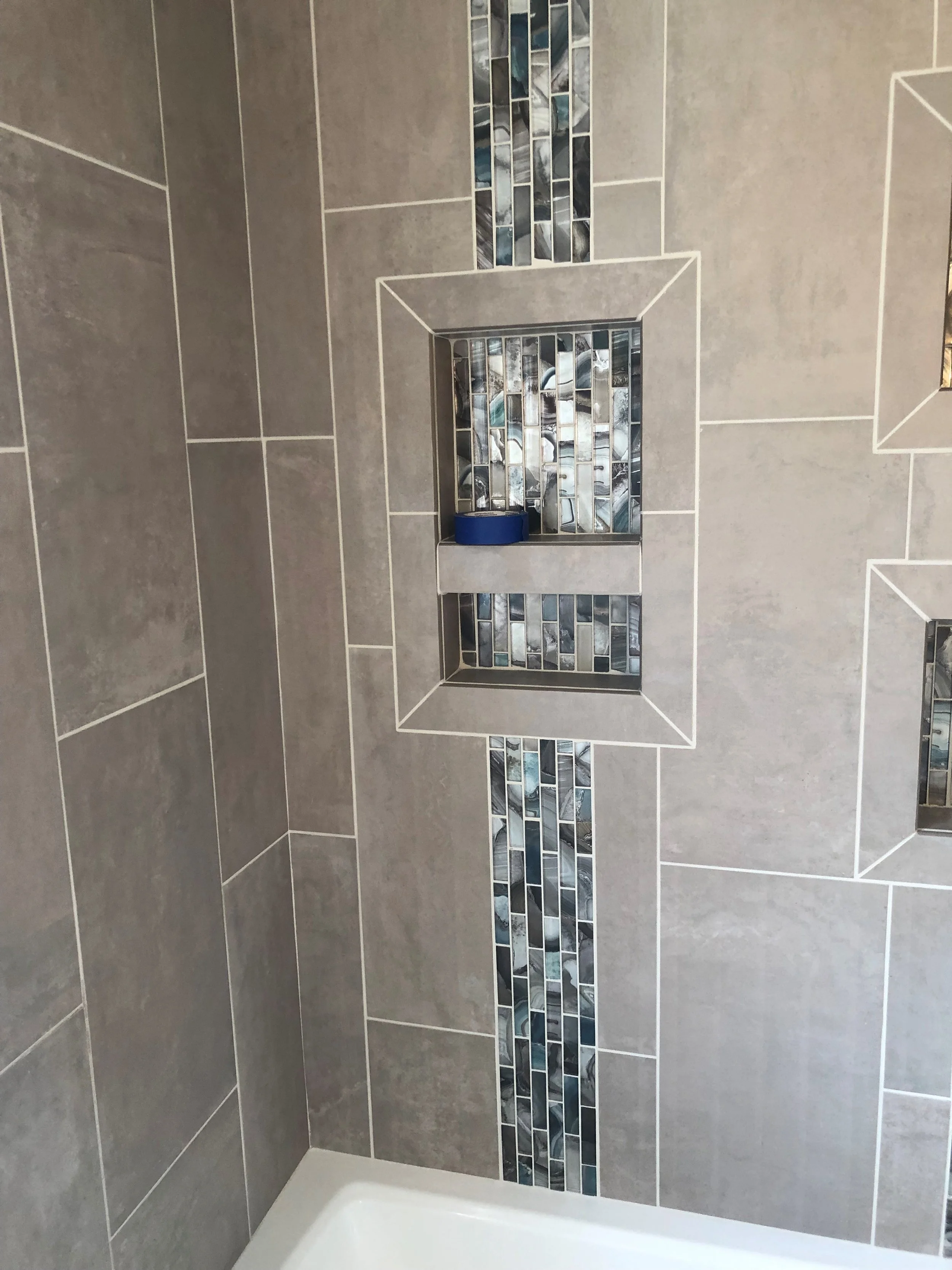 Bathroom shower wall with gray tiles and blue mosaic accent tiles, featuring a built-in niche.